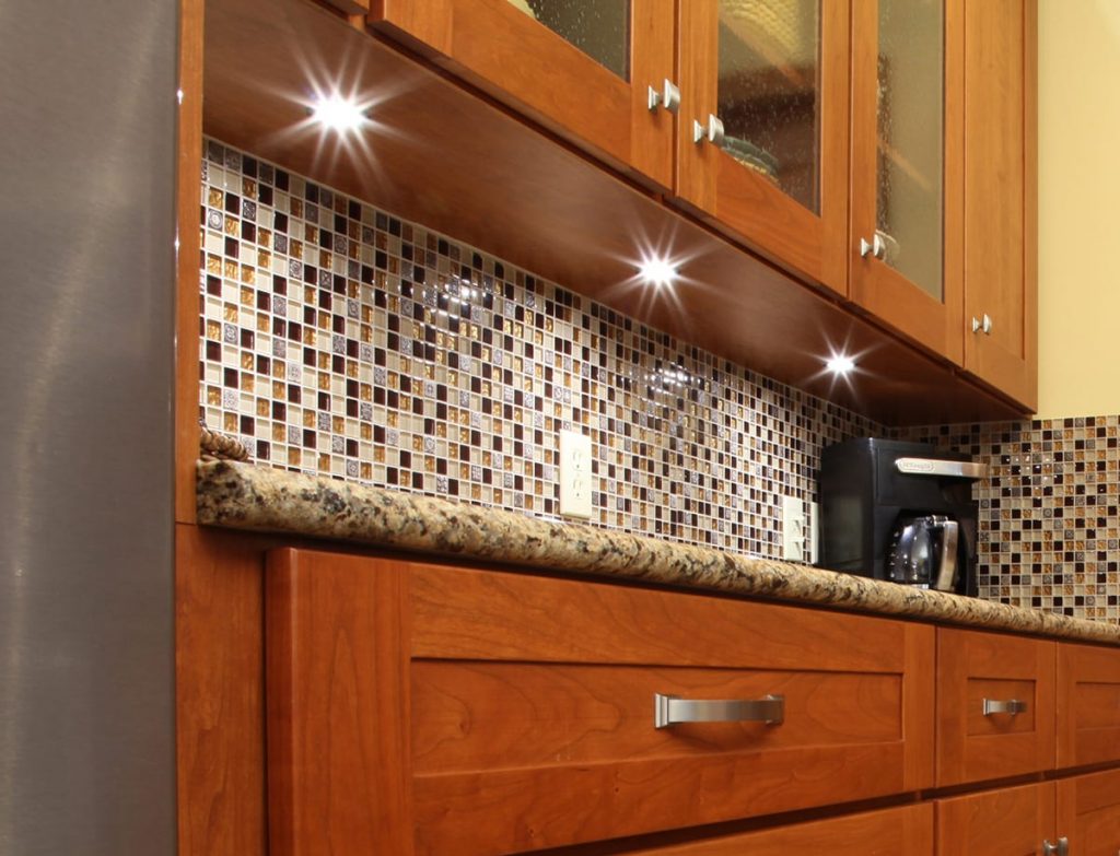 Kitchen cabinet with under-cabinet lighting, featuring light wood doors, drawers, and a dark countertop.