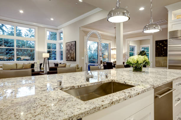 White kitchen design features large bar style kitchen island with granite countertop illuminated by modern pendant lights