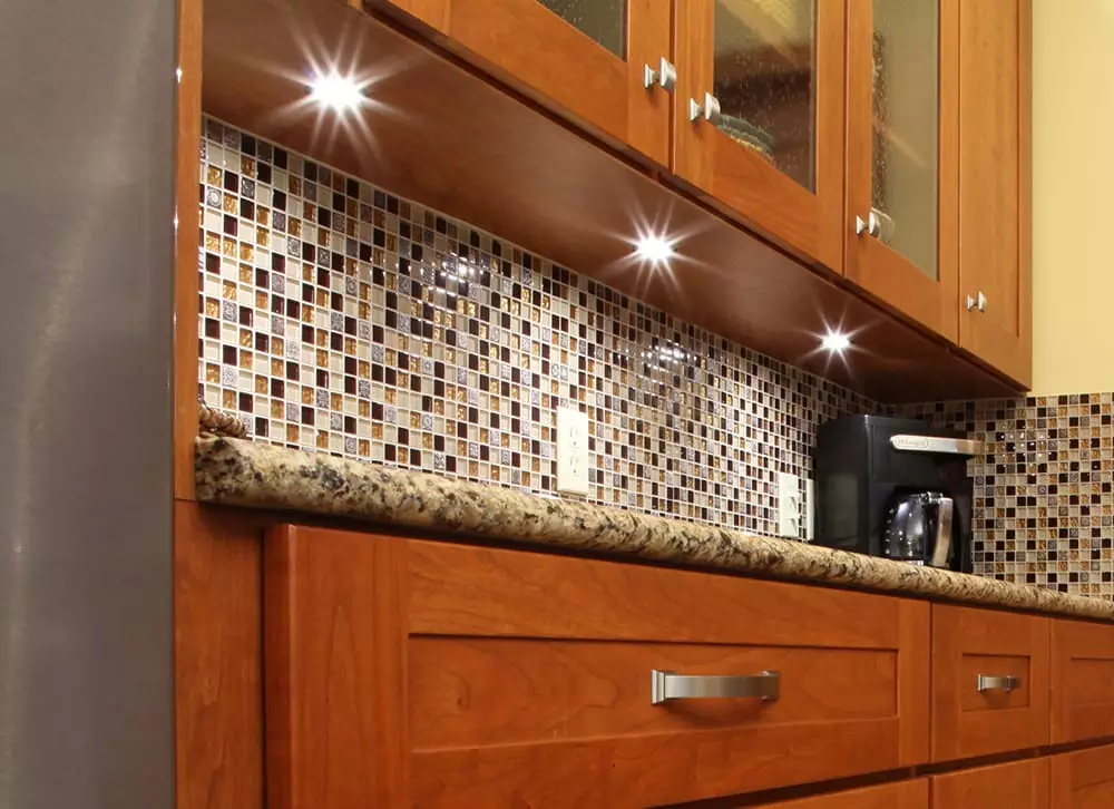 Kitchen cabinet with under-cabinet lighting, featuring light wood doors, drawers, and a dark countertop.
