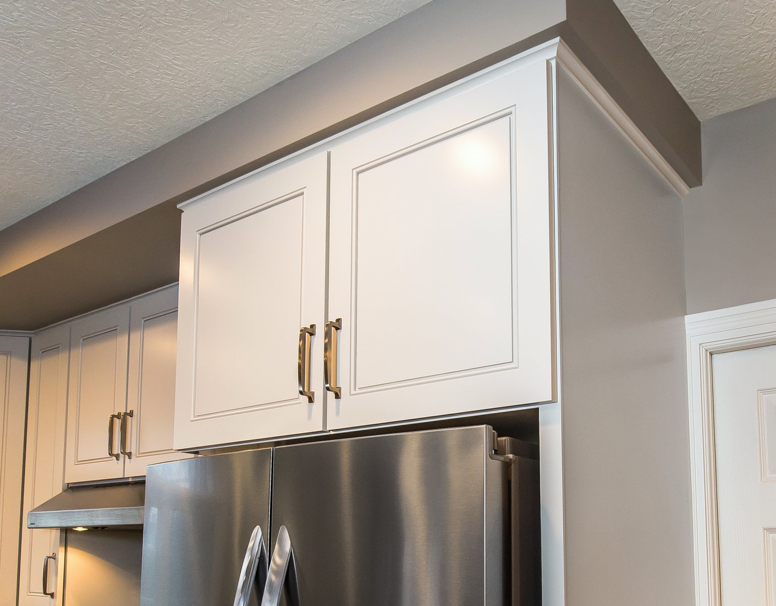 White refaced kitchen cabinets above a silver refrigerator