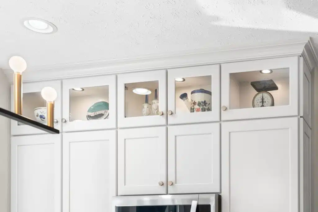 Refaced white kitchen cabinets extended to the ceiling with lighted glass-door uppers