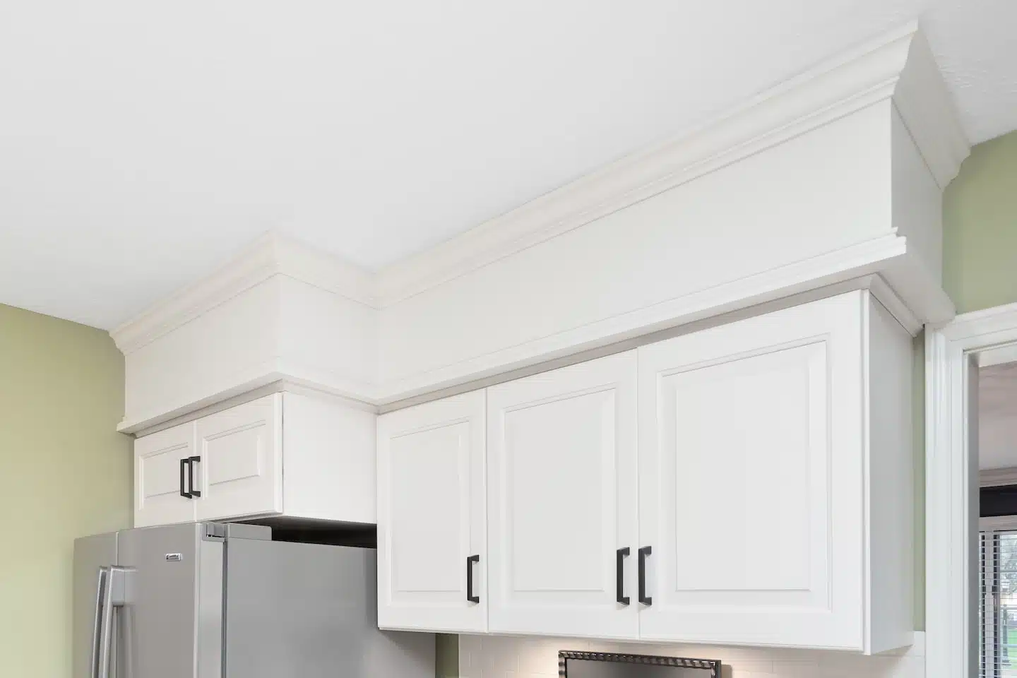White upper kitchen cabinets featuring thick decorative crown molding that seamlessy bridges the space between the cabinet tops and the ceiling.