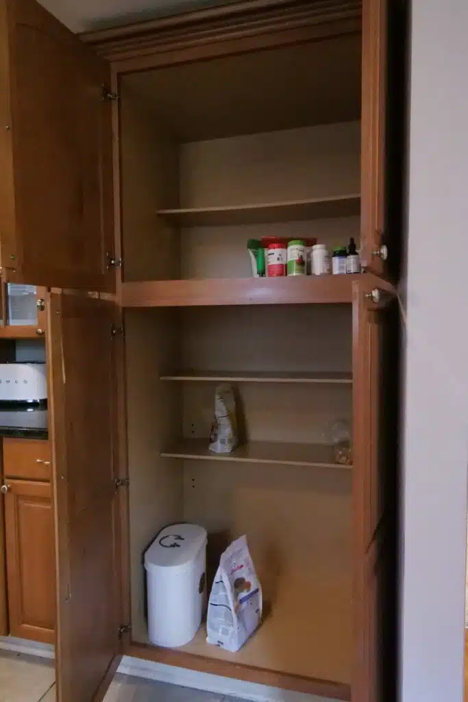 Open, dated wood pantry cabinet with static shelves sparsely holding a few grocery items.
