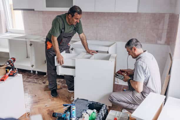 Workers working on cabinet refacing in the kitchen area.