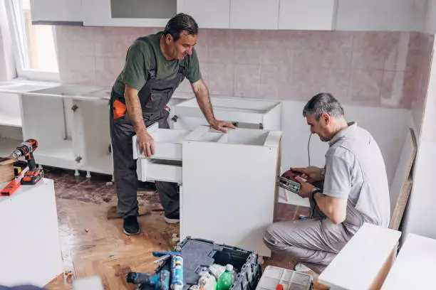 Workers working on cabinet refacing in the kitchen area.