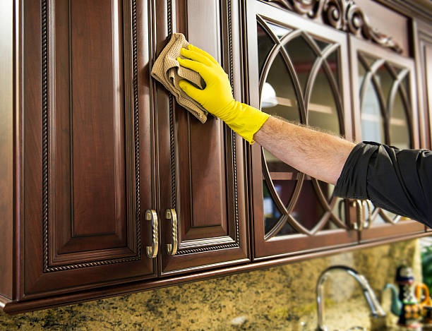 A man cleaning a wooden kitchen cabinet.