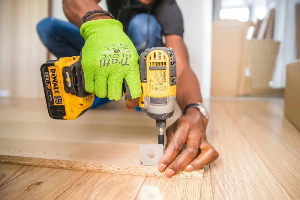 Handyman securing a cabinet panel with a drill during a cabinet refacing project, promoting reuse of existing materials instead of disposal.
